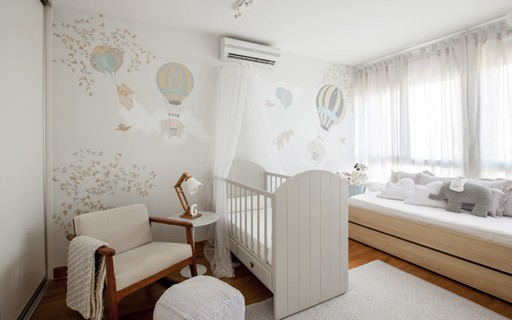 Quarto de bebê claro com berço branco, poltrona bege e decoração com balões na parede.
