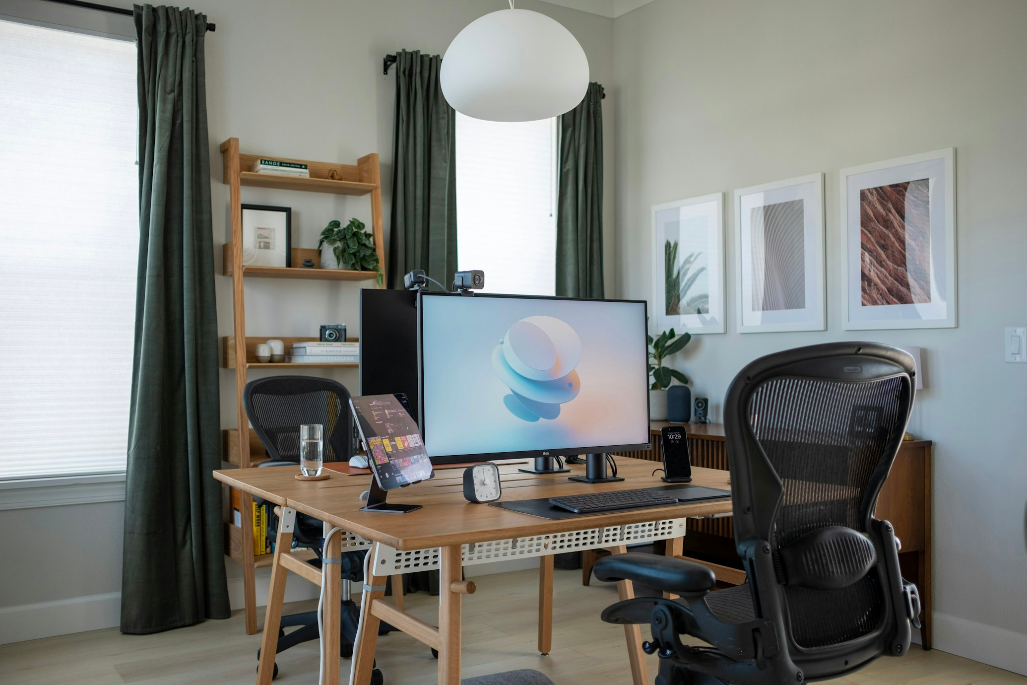 Escritório bem iluminado com mesa de madeira, cadeira ergonômica preta e monitor grande.