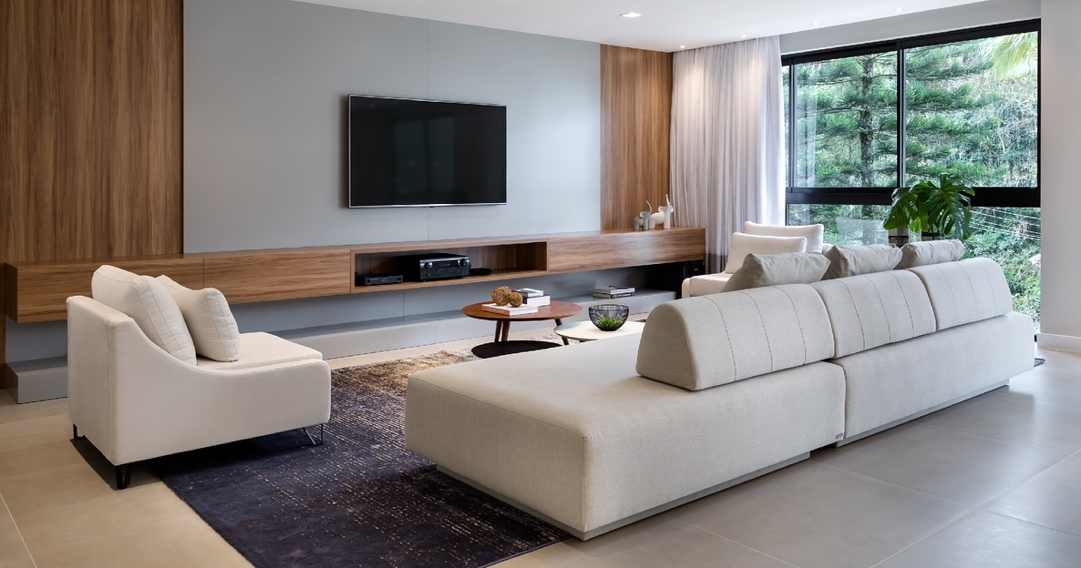 Sala de estar moderna com sofá cinza, tapete estampado e painel de TV de madeira.